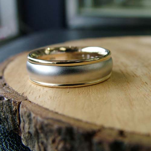 Custom men’s engagement ring in yellow gold with a brushed center and polished edges on a wood slice.