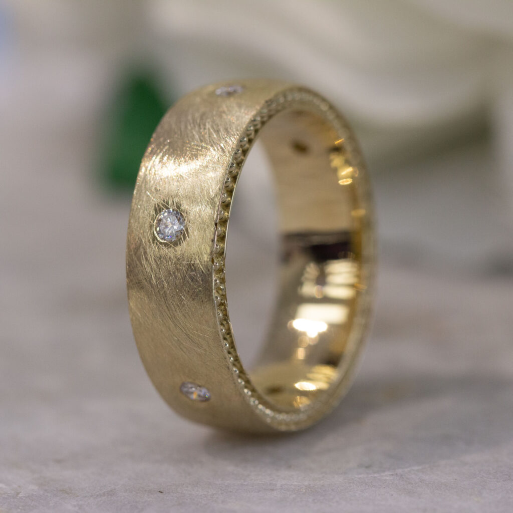 Custom men’s engagement ring in yellow gold with a brushed texture and flush-set diamond accents.