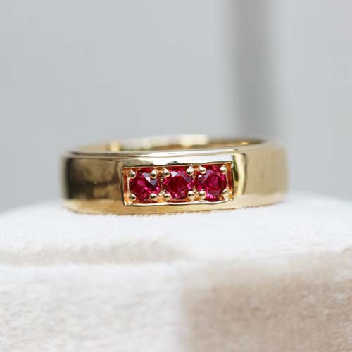 Custom men’s engagement ring in yellow gold featuring a row of red gemstones set in a bold band.