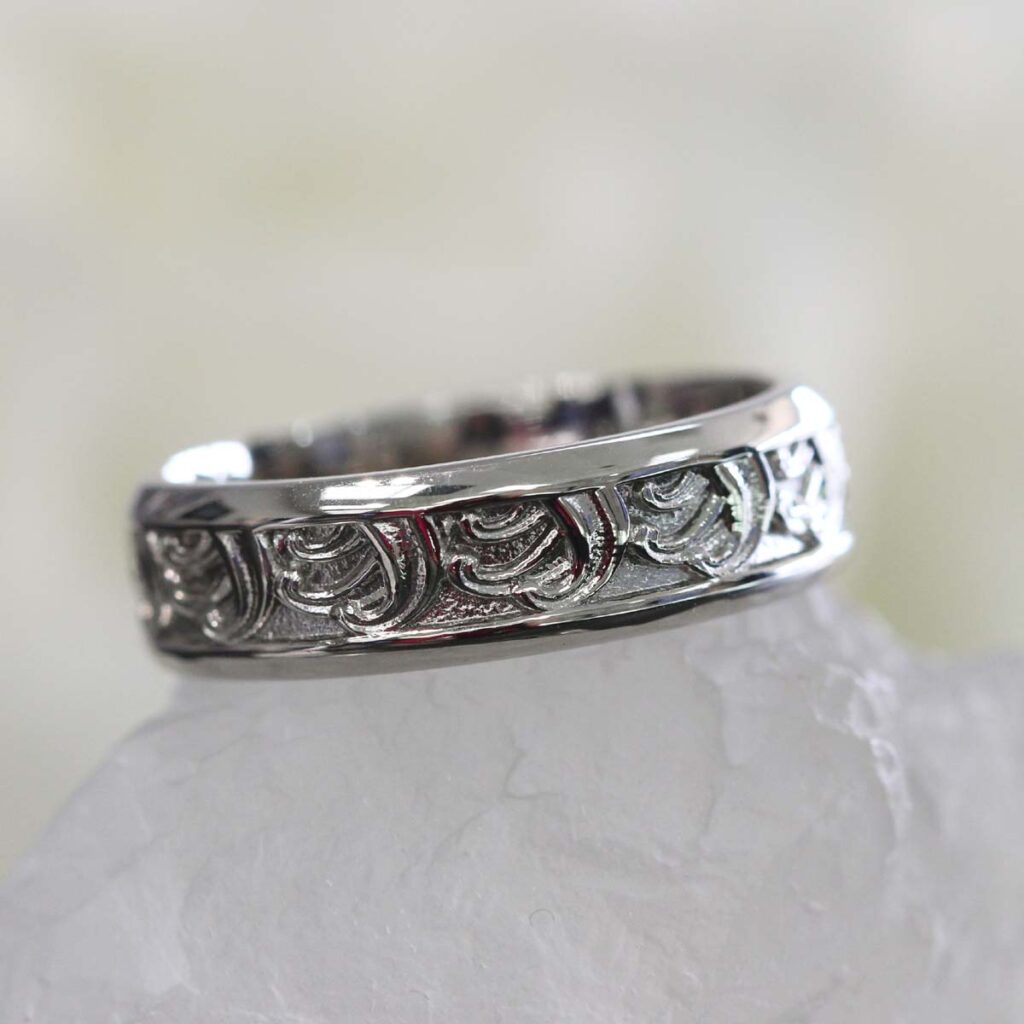 Custom men’s engagement ring in white gold with intricate engraved detailing around the band.