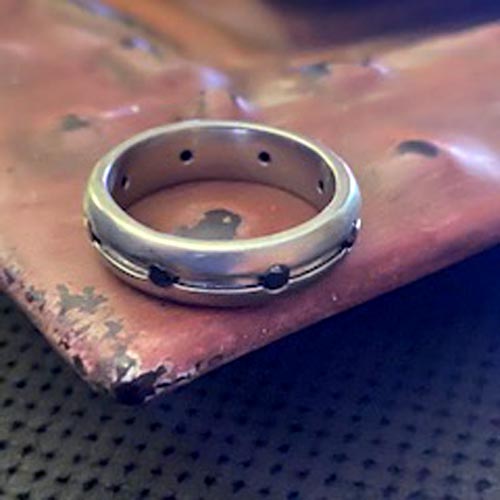 Custom men’s engagement ring in mixed metals with a brushed finish and dark accent rivets.