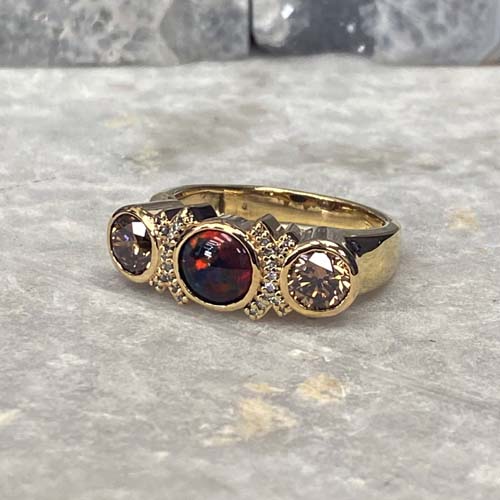 Unique custom men’s engagement ring in yellow gold with bezel-set opal and diamond accents.